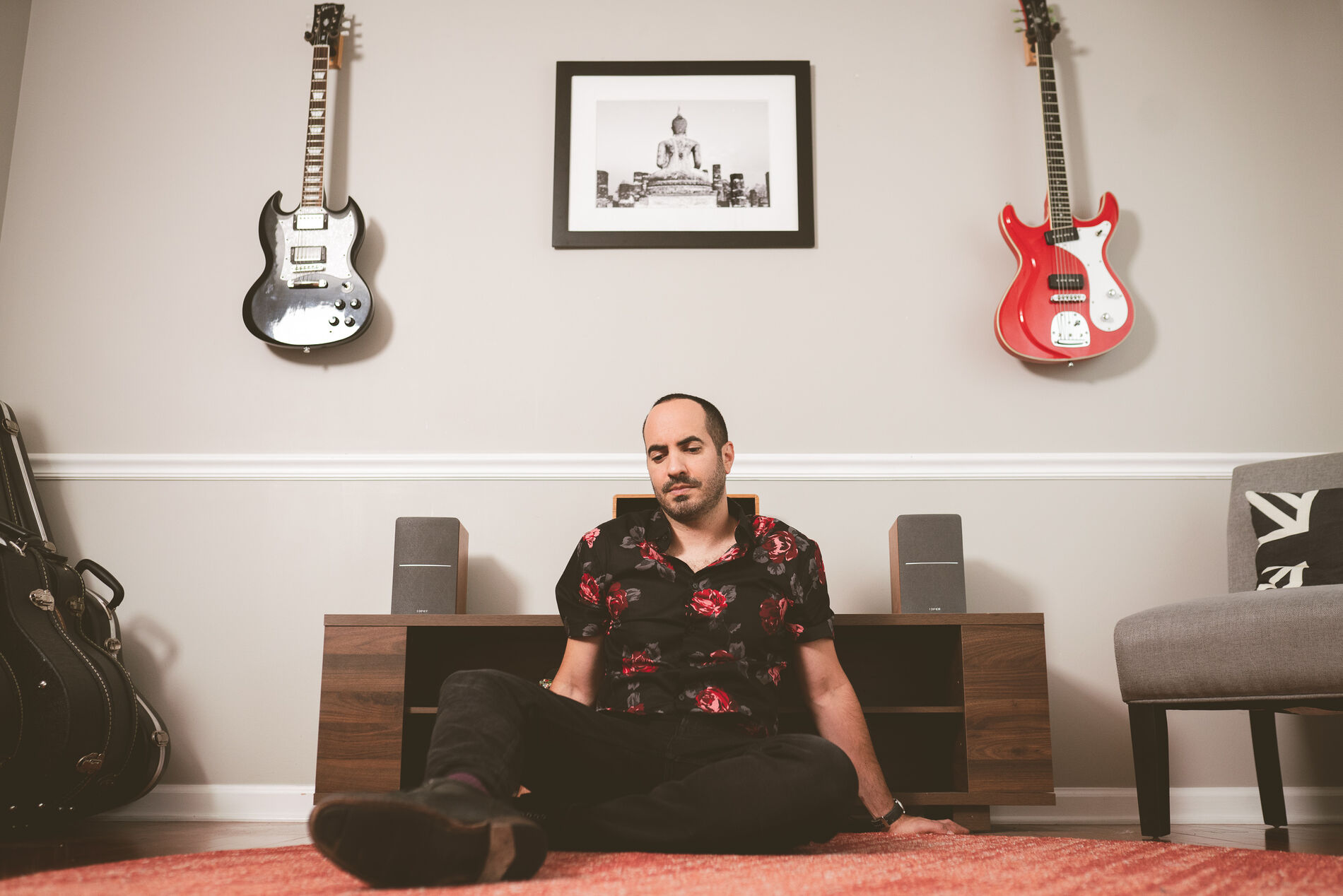 SOHEILL seated on the floor of his living room between two electric guitars mounted on the wall.